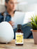 Bottle of vanilla fragrance oil next to a diffuser on a table with a blurred person in the background.