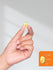 Hand holding a yellow supplement capsule with size measurement details on a gray background