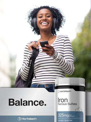 View 6 Woman smiling with headphones and holding smartphone, alongside Horbaach Iron Ferrous Sulfate bottle.