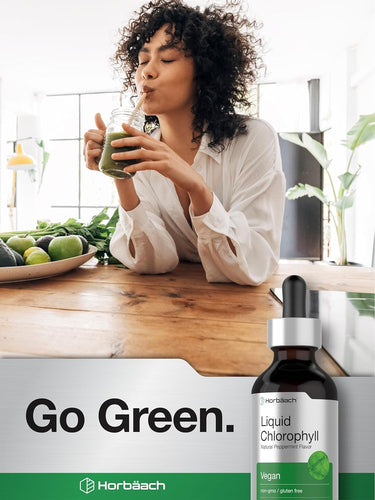 Woman drinking green juice with a bottle of Horbaach Liquid Chlorophyll on a kitchen counter.