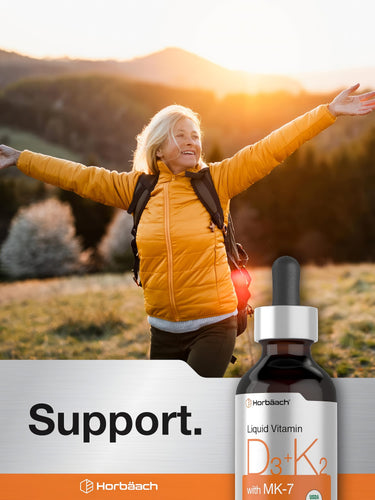 View 6 Older woman hikes outdoors with arms outstretched at sunset beside a Horbäach Liquid Vitamin D3 + K2 bottle.