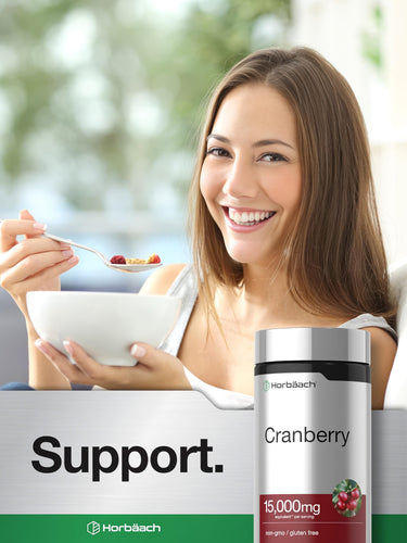 View 6 Young woman smiling while eating cereal with a Horbäach Cranberry supplement bottle beside her.