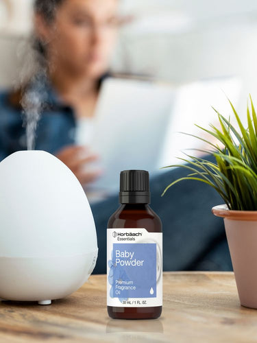 View 4 Bottle of Horiba Baby Powder fragrance oil on a table with a diffuser and plant in the background.