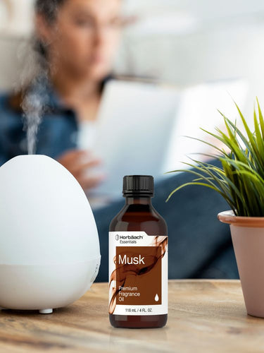 Bottle of Musk premium fragrance oil next to a diffuser on a table with a blurred person in the background.