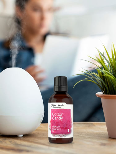 Bottle of Cotton Candy fragrance oil on a table with a diffuser and plant in the background.
