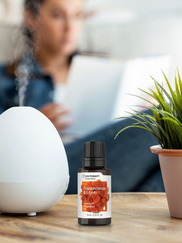 Bottle of Frankincense & Mint essential oil with a diffuser and plant on a table.