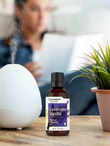 View 4 Bottle of lavender vanilla fragrance oil on a table with a diffuser and plant in the background.