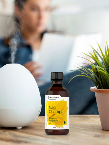 Nag Champa fragrance oil bottle on a table with a person and plant in the background.