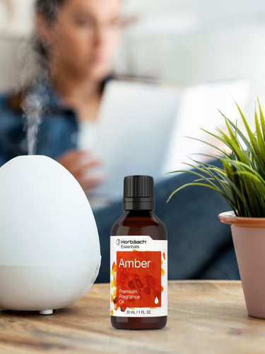 View 4 Bottle of premium fragrance oil on a table with a diffuser and plant in the background.