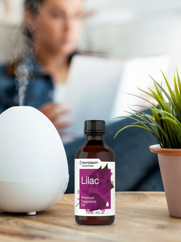 View 4 Bottle of lilac fragrance oil on a table with a diffuser and plant in the background.