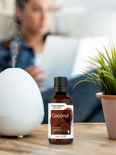 Bottle of coconut fragrance oil next to a diffuser on a table with a blurred background
