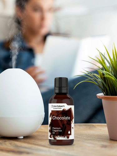 View 4 Bottle of chocolate fragrance oil on a table with a person and plant in the background.