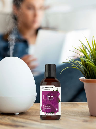 View 4 Bottle of lilac fragrance oil on a table with a diffuser and plant in the background.