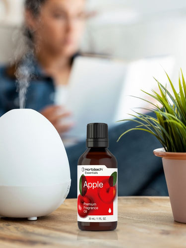 View 4 Bottle of apple fragrance oil on a table with a diffuser and plant in the background.