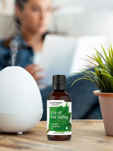 Bottle of Herbals Lily of the Valley fragrance oil on a table with a diffuser and plant in the background.