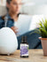 Bottle of lavender oil with a diffuser and plant on a table, person using laptop in background