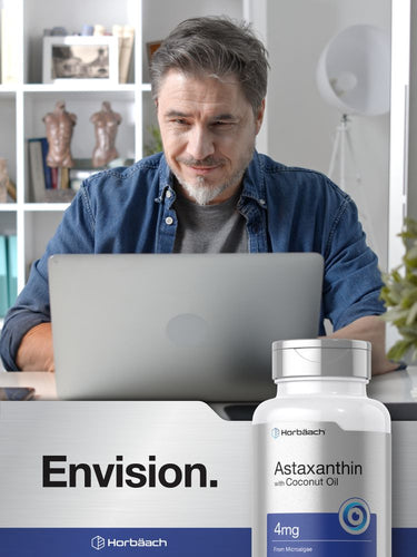 Man using a laptop with a bottle of Hertäbach Astaxanthin supplement in the foreground.
