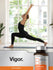 Person doing yoga in a bright room with a bottle of vitamins on a table.