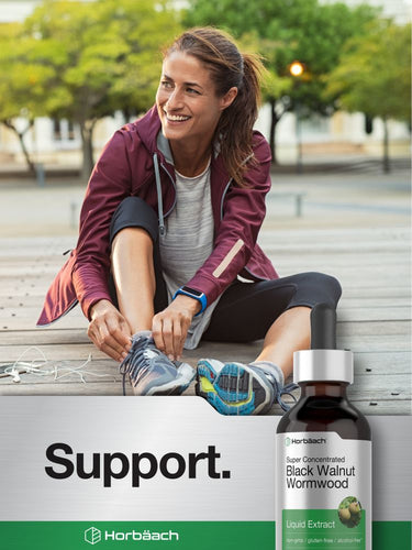 View 6 Woman sitting on a bench with a bottle of Black Walnut Wormwood extract.