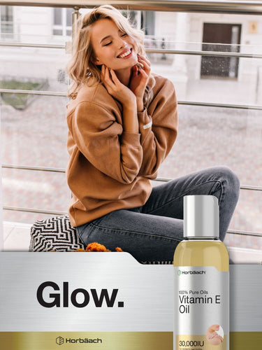 View 6 Woman smiling on a balcony with a bottle of vitamin E oil in the foreground.