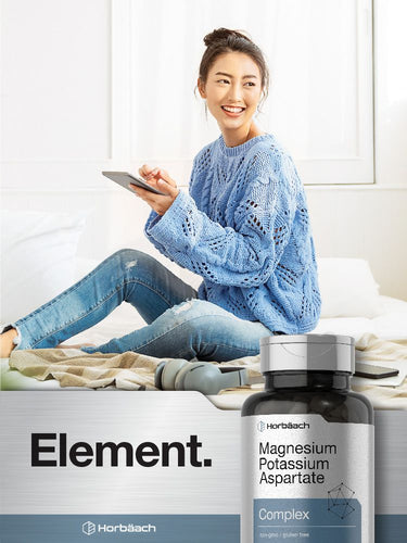 View 6 Person sitting on a bed using a smartphone with a bottle of magnesium potassium aspartate in the foreground.