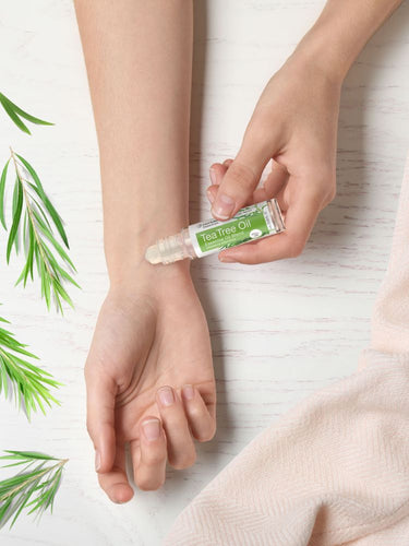 View 8 Person applying Tea Tree Oil to their wrist with green leaves on a light background