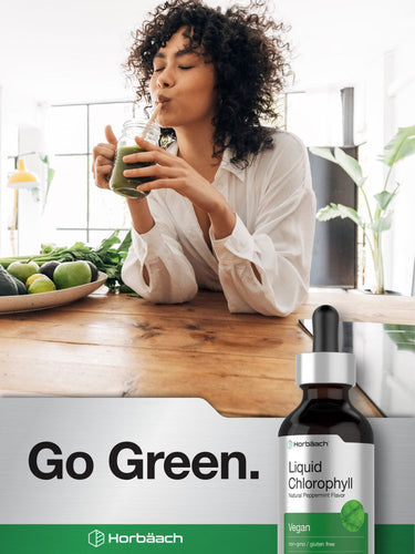 Woman drinking green juice with a bottle of Horbaach Liquid Chlorophyll on a kitchen counter.