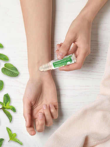 View 6 Person applying peppermint oil to wrist with mint leaves on white background