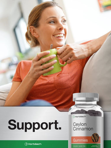 Woman sitting on a couch holding a green mug with Ceylon cinnamon gummies and a bottle of gummies in the foreground.