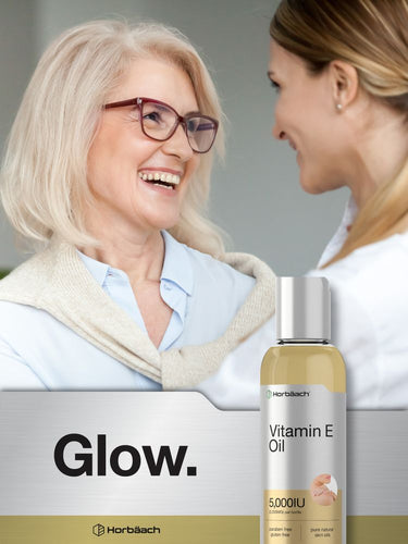 Two women smiling with a bottle of vitamin E oil in the foreground.