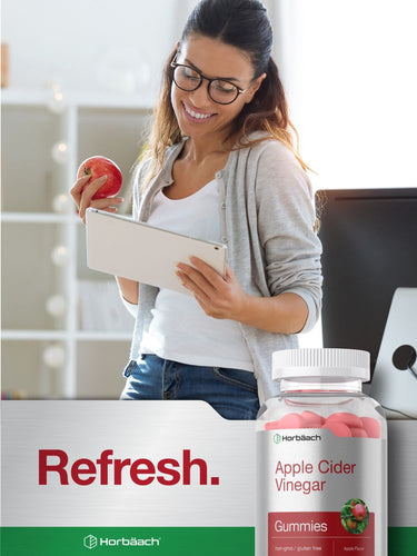View 8 Woman using a tablet with a bottle of apple cider vinegar gummies in the foreground.