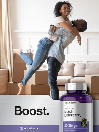 Couple celebrating in a living room with moving boxes and a bottle of Sambucus Black Elderberry supplement.