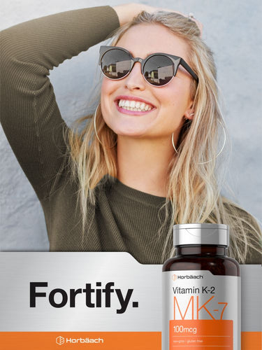 View 6 Woman smiling with a bottle of vitamin supplement in the foreground.