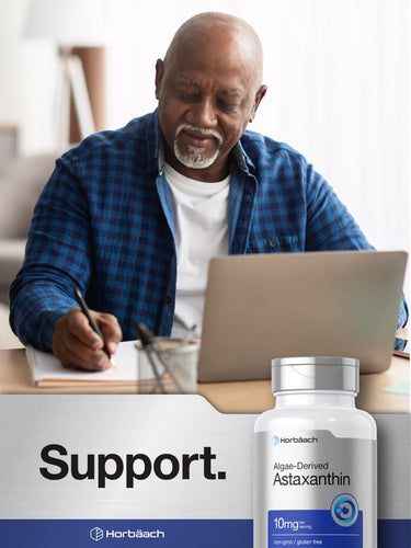 Man using laptop with Astaxanthin supplement bottle on table.