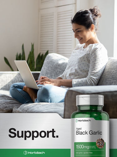 Woman using a laptop on a couch with a bottle of black garlic supplement in the foreground.