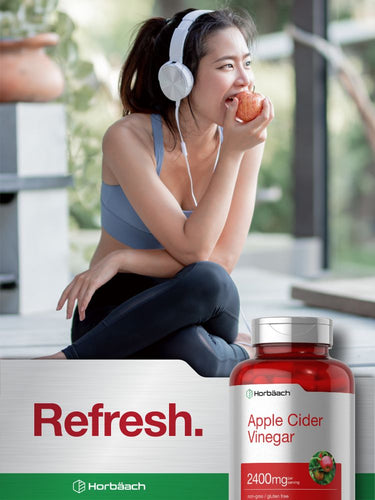 Person sitting with apple and headphones, apple cider vinegar bottle in foreground