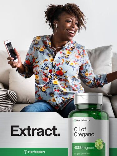 Woman sitting on a couch holding a phone with a bottle of Oil of Oregano in the foreground.