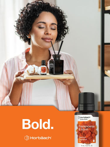 Woman holding a tray with diffusers and a bottle of Herbäach Frankincense & Myrrh oil, with 'Bold.' branding.