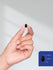 Hand holding a small black object with a measurement inset on a light gray background