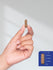 view 7 Hand holding a capsule with a size reference on a gray background
