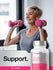 Woman exercising with pink dumbbells and a bottle of Women's Multi 50+ supplement.