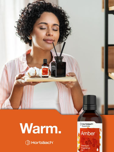 View 7 Person holding a tray with fragrance bottles and a bottle of amber fragrance on an orange background.