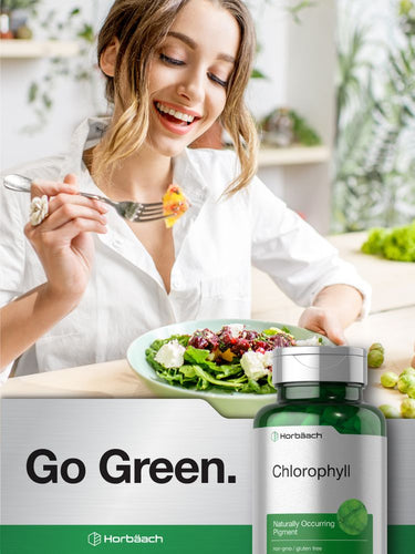 Woman enjoying a salad with a bottle of chlorophyll supplement in the foreground.