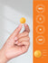 Hand holding a yellow supplement capsule with branding and certification logos on an orange background