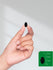 Hand holding a black seed with size reference on a green square