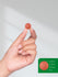 Hand holding a small red object with a size reference on a green background.