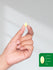 Hand holding a pill with a size reference on a gray background