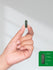 Hand holding a green capsule with size reference on a white background