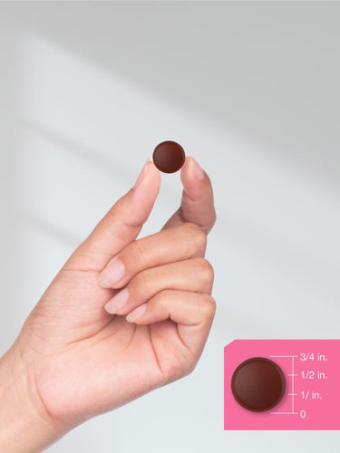 Hand holding a small brown chocolate against a plain background.