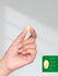 Hand holding a yellow supplement capsule with size measurement inset.